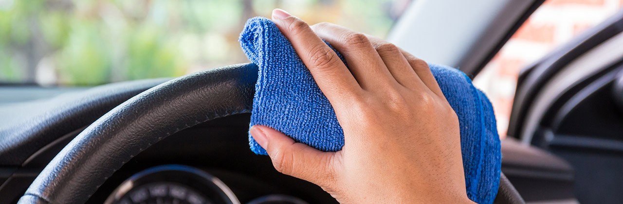 A hand uses a microfiber cloth to clean a car steering wheel