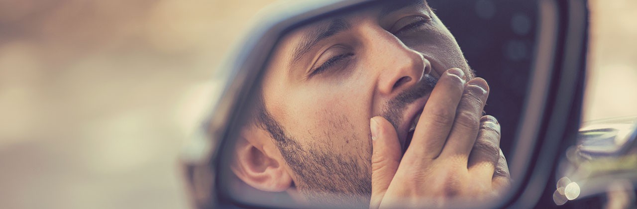 Male driver yawning while driving, as seen in rear-view mirror