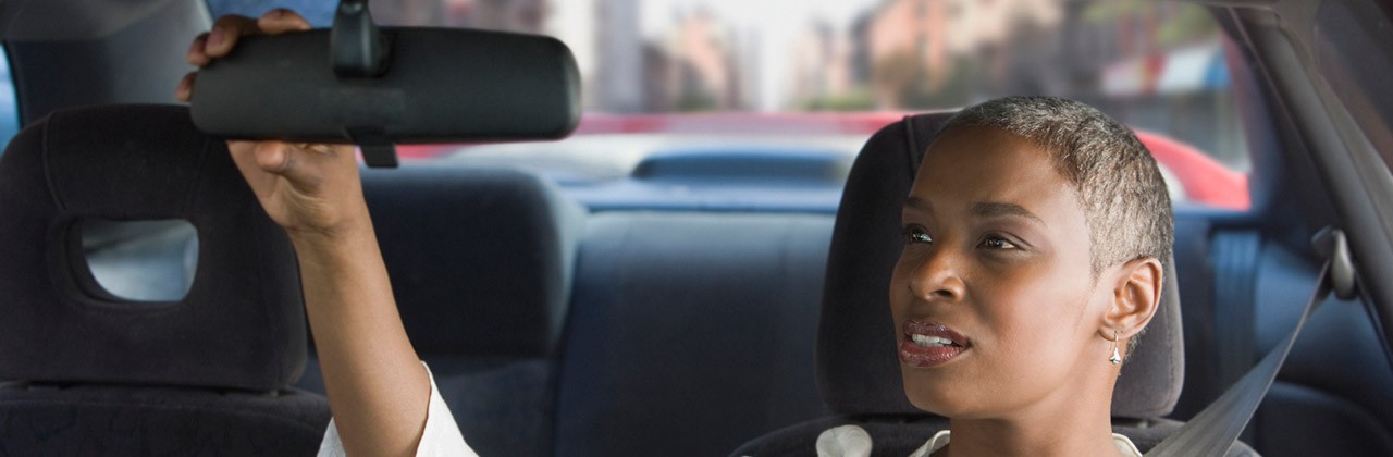 Woman driver adjusting rear-view mirror in car