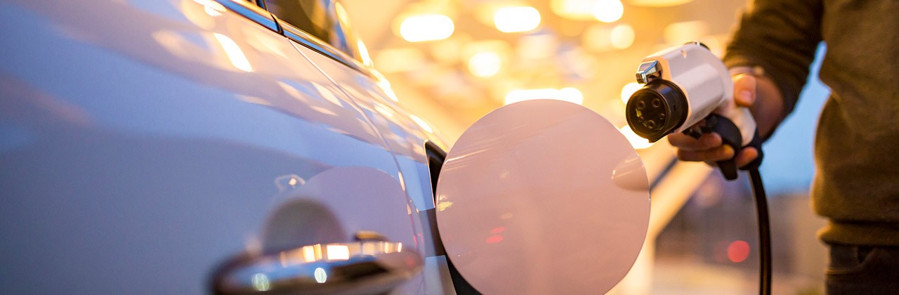 A person approaches an electric car holding a charging cable plug