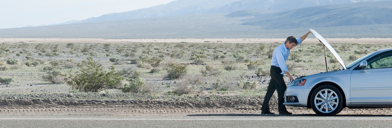 A man looking under the hood of his car on the side of the road