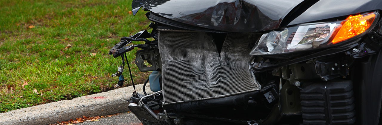 The front hood of a black car that has been wrecked, with the bumper missing and the radiator hanging out