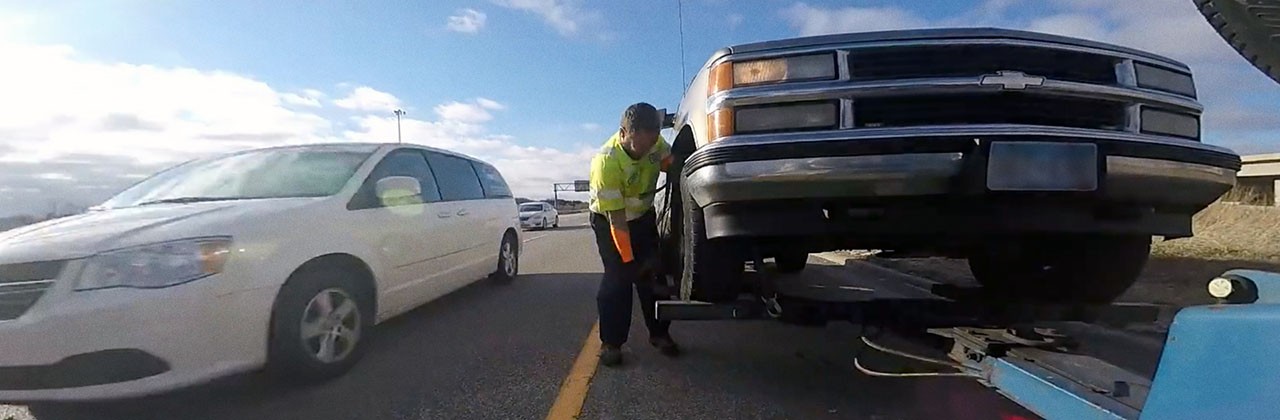 A roadside assistance technician hitching up an SUV to be towed by a tow truck