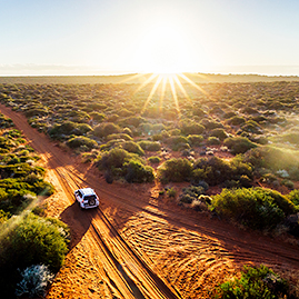 Car driving along an unpaved red-sand road