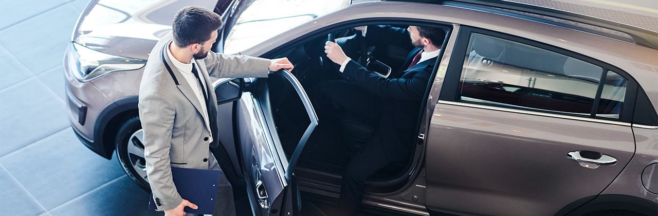 Car salesman opening door for customer getting into his brand new luxury car