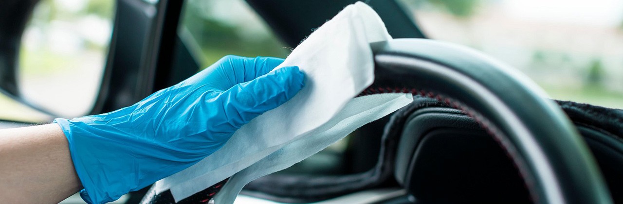A gloved hand cleaning a steering wheel of a car.