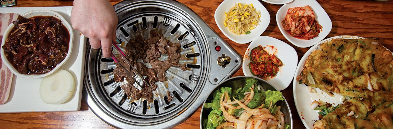 A spread of Korean food including side dishes and meat cooking on a tabletop grill at So Gong Dong Tofu & BBQ