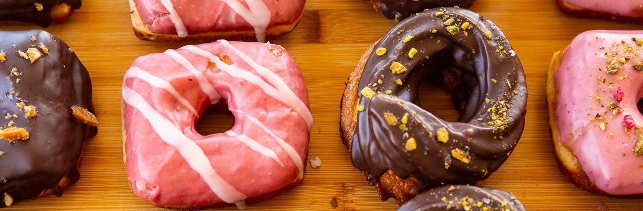 Square and round doughnuts with various toppings including nuts, toffee, and drizzles