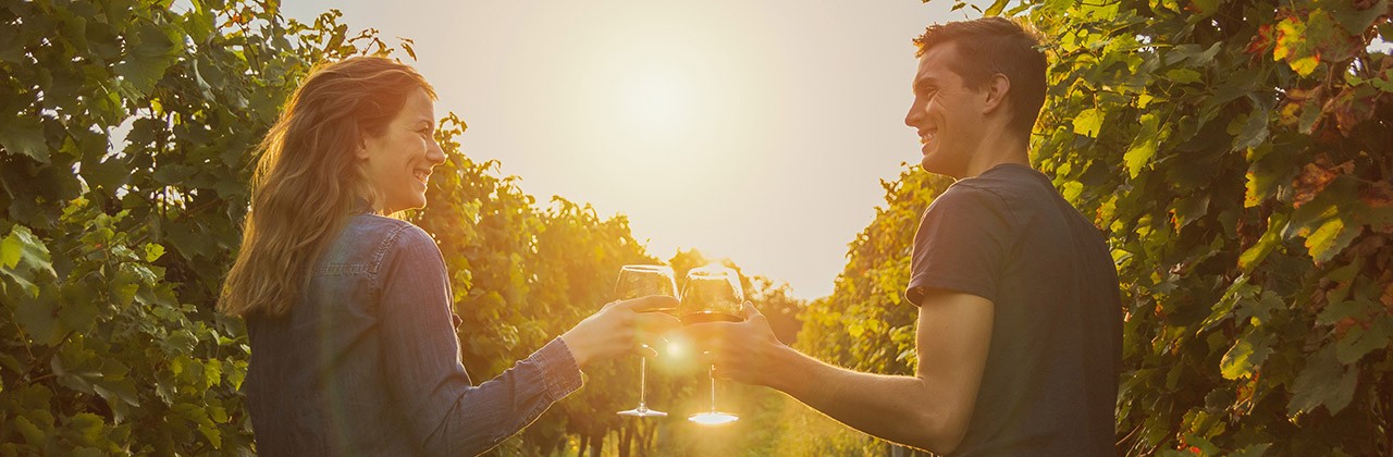 woman with denim shirt and man with t-shirt drinking red wine during sunset. 
