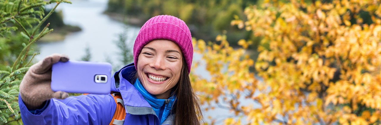 Happy asian hiker woman taking smartphone selfie at scenic viewpoint in nature fall mountain landscape outdoors. Girl hiking in Autumn forest park travel lifestyle. Girl holding phone.