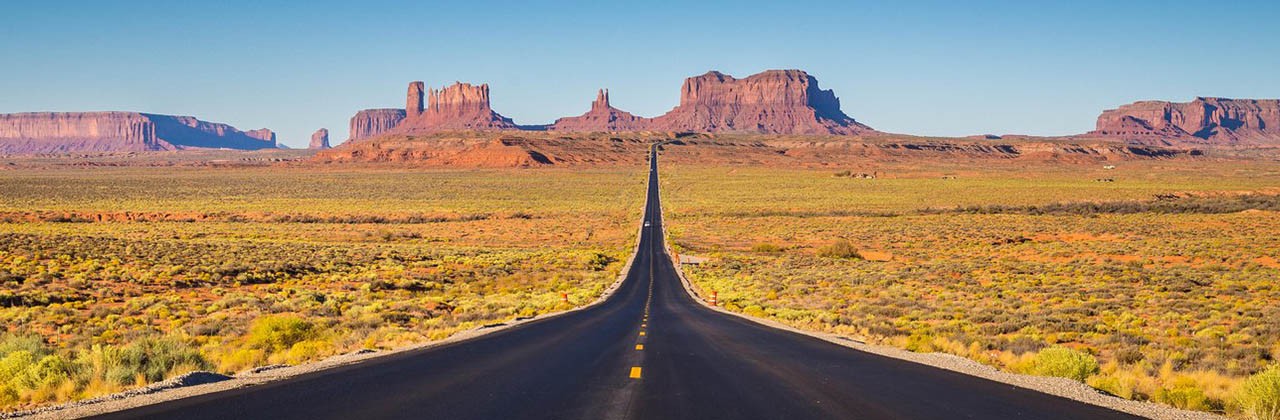 Classic panorama view of historic U.S. Route 163 running through famous Monument Valley in beautiful golden evening light at sunset, Utah, USA
