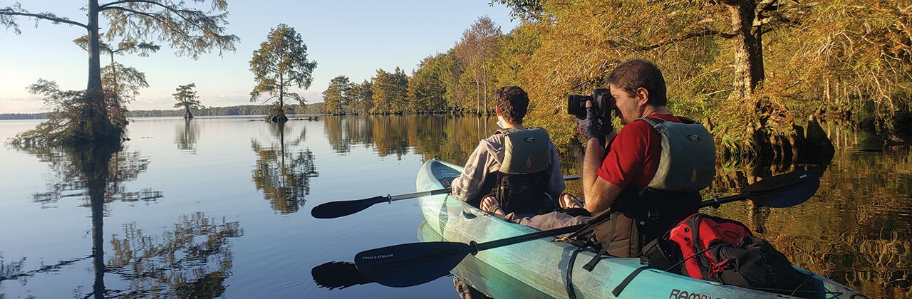 Pair of kayakers, one taking a photograph, in Great Dismal Swamp