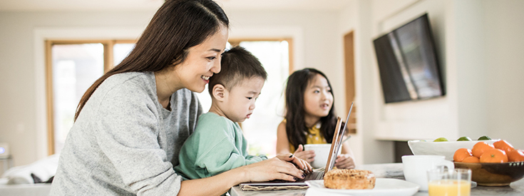 Mother with child sitting on lap looking at laptop screen