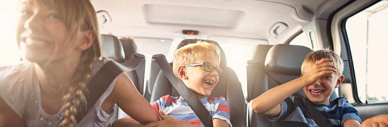Three kids playing and laughing in the back seat of a car