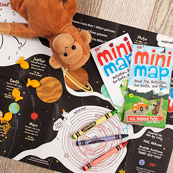 A stuffed monkey on top of mini maps and crayons
