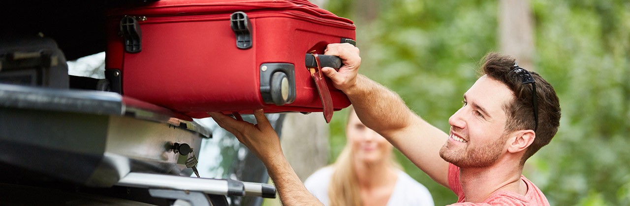 Dad loading suitcase onto the roof ahead of a road trip