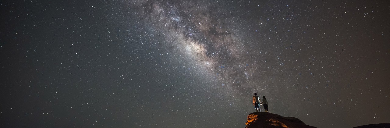 Couple stargazing under the Milky Way on a rock