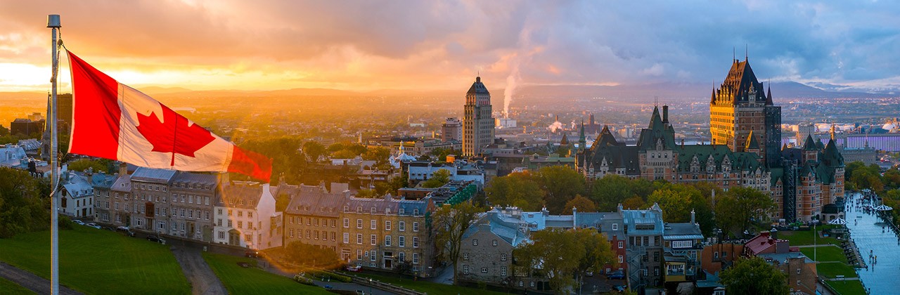 A Canadian flag waves above Quebec City at sunset, including Le Chateau Frontenac.