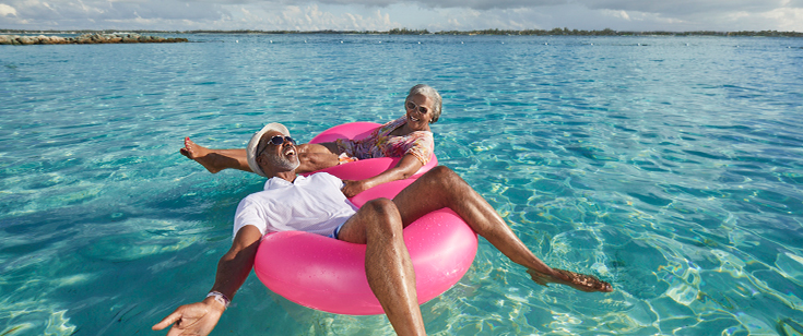 Couple floating in pink innertubes in ocean