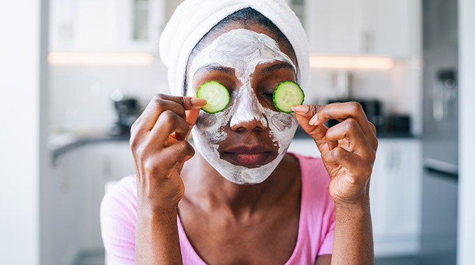 A woman applies face cream and cucumber slices to her face