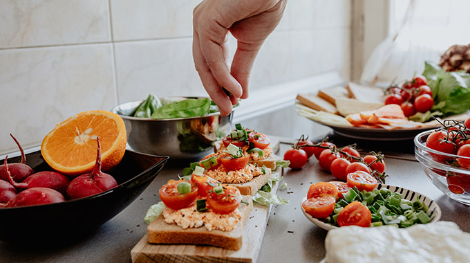 A person makes bruschetta with a number of fresh ingredients