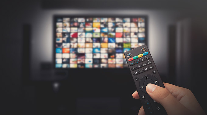A hand holding a remote control in front of a smart TV