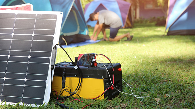 A solar panel charging a phone outside tents on a camping trip