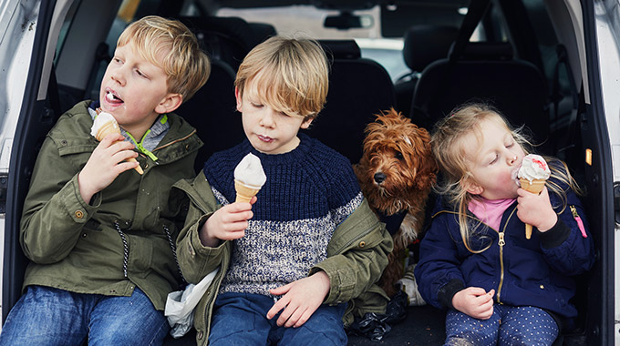 Three kids and a dog in the back of a car, with the kids eating ice cream