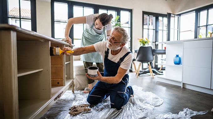 An older man and his daughter renovating a home by painting furniture
