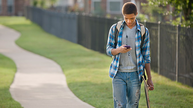 A teenage boy walking while looking at a smartphone