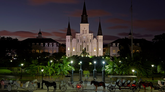 Horse-drawn carriages wait in front of Jackson Square at night in New Orleans