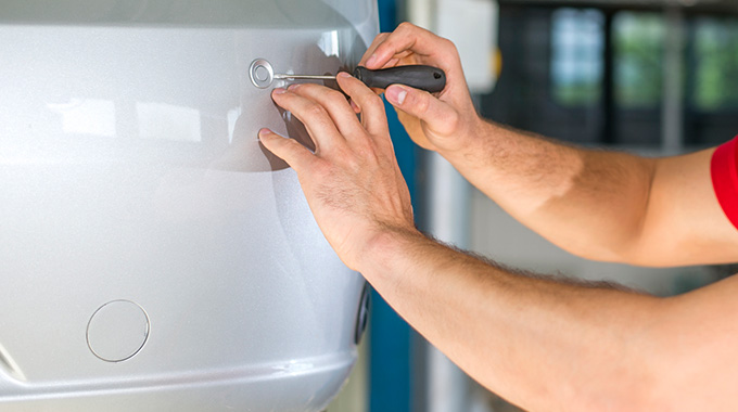 A technician uses a screwdriver to pop a sensor cover off a car bumper