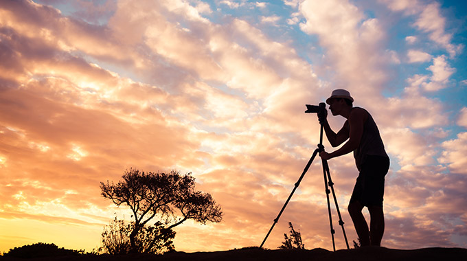 A man with a camera on a tripod photographing a sunset