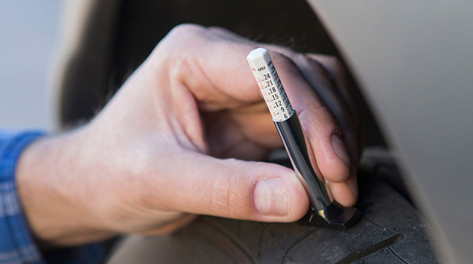 Hand measuring tire tread depth with a depth gauge