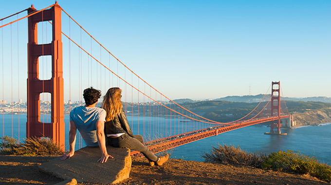 A couple sits on a rock overlooking the Golden Gate Bridge