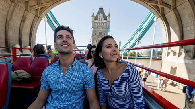 Young couple riding on top deck of an open tour bus going over the Tower Bridge in London
