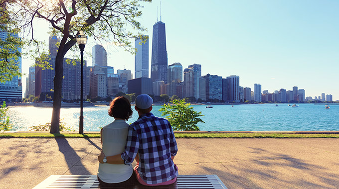 A couple sits on a bench overlooking the Chicago skyline and Lake Michigan