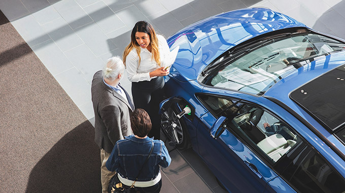 A saleswoman talks to two customers about an electric vehicle at a dealership showroom