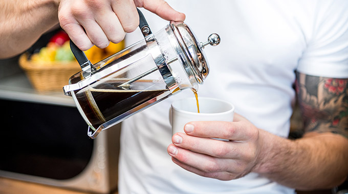 A man pours French press coffee into a mug