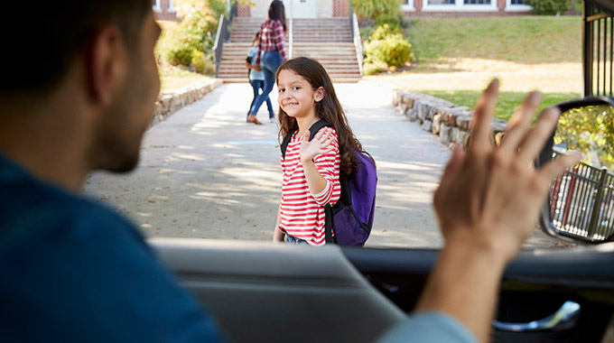 A dad in a car waves to a little girl he has dropped off