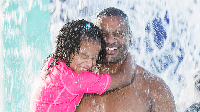 A father and daughter stand under a waterfall at a water park