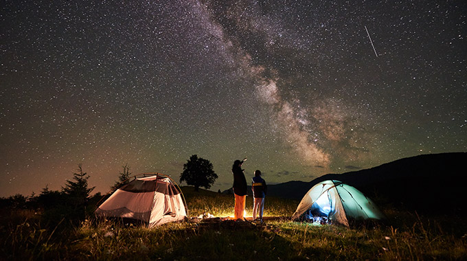 A mother and son look at the Milky Way in the night sky while camping outdoors with tents