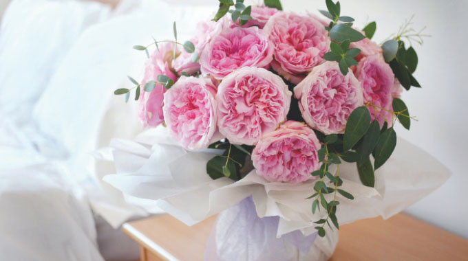 A bouquet of pink roses in a wrapped gift vase placed on a bedside table