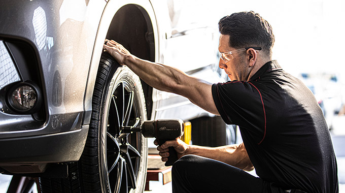 A mechanic uses a power tool to work on a car wheel with new tires