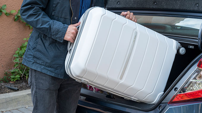 A white Samsonite suitcase being loaded into the trunk of a car