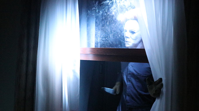 A scareactor comes through a window with a knife in a maze at Universal Studios Hollywood Halloween Horror Nights
