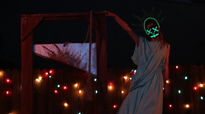 A scareactor dressed as the Statue of Liberty with a neon mask stands next to a guillotine in the Terror Tram maze