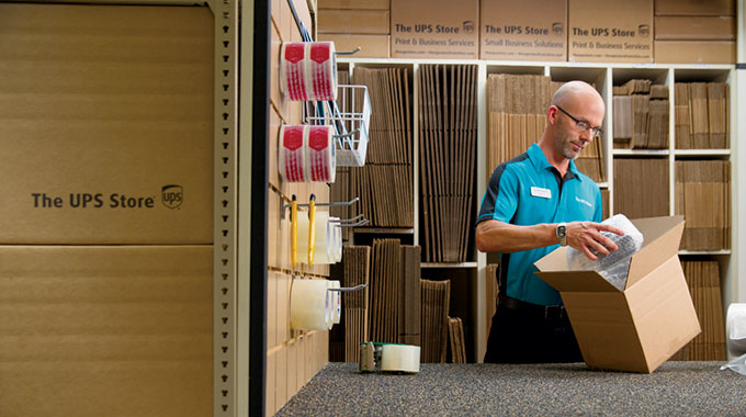 A UPS Store associate packs an item covered in bubble wrap into a cardboard box