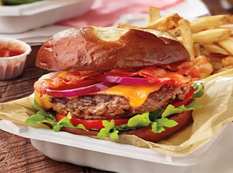 A burger with a pretzel bun and fries in a delivery container from Grubhub