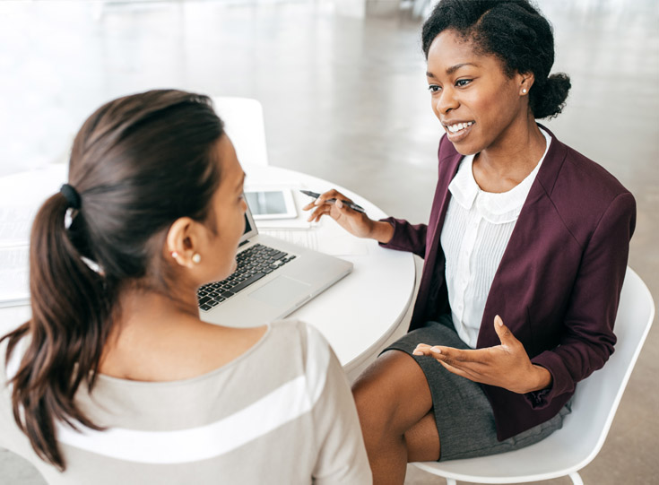 Insurance agent facing AAA member next to a table with a laptop explaining coverage Insurance agent facing AAA member next to a table with a laptop explaining coverage